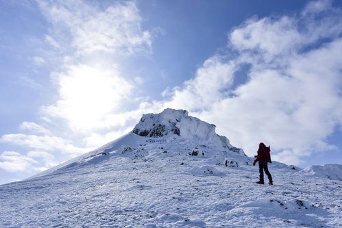 安達太良山の雪山山頂を眺める赤いウェアの登山者