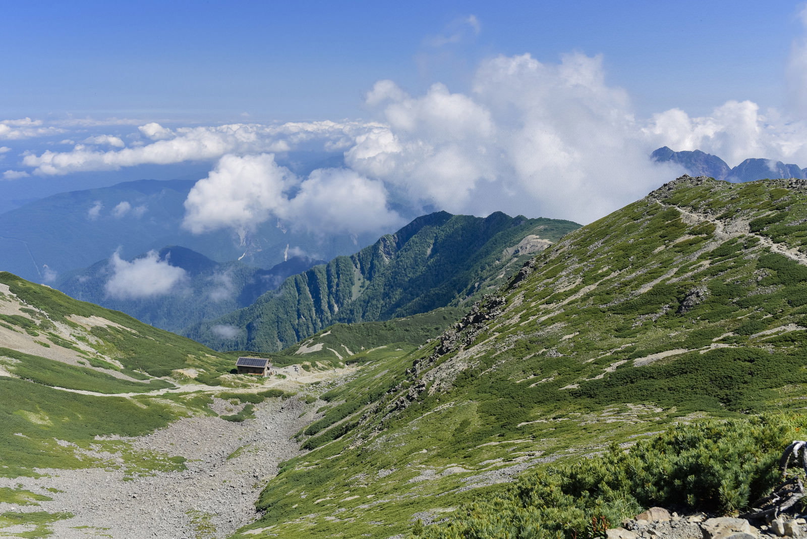 仙丈ヶ岳の稜線に建つ山小屋と青空に湧き上がる白い雲