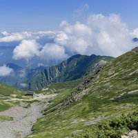 仙丈ヶ岳の稜線に建つ山小屋と湧き上がる雲の写真
