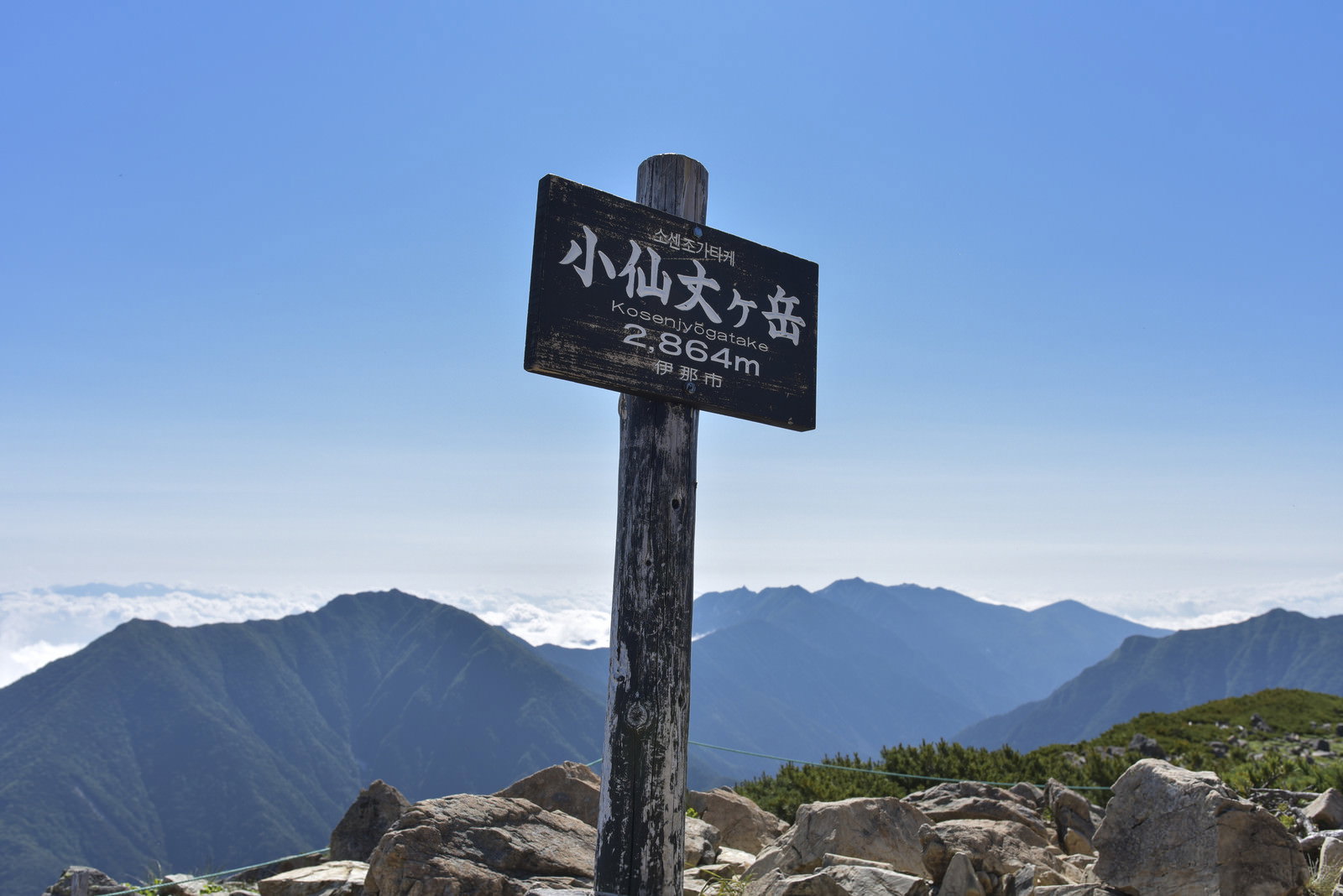 岩場に立つ小仙丈ヶ岳の山頂標と山々の稜線