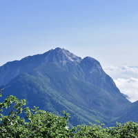 青空の下、緑の樹木越しに望む甲斐駒ヶ岳と仙丈ヶ岳の写真