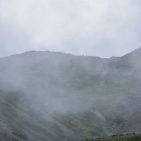 雲に包まれる仙丈ヶ岳の稜線を歩く登山者たちの写真