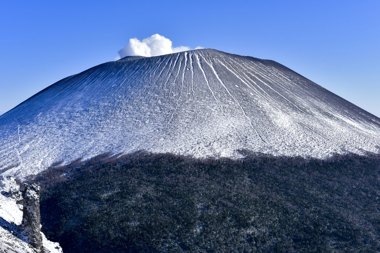 青空の下で雪化粧した浅間山、山頂から噴煙が立ち上る