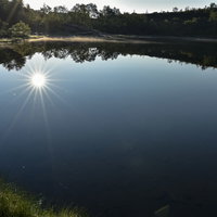 草津白根山の弓池に映り込む太陽と光芒の風景の写真