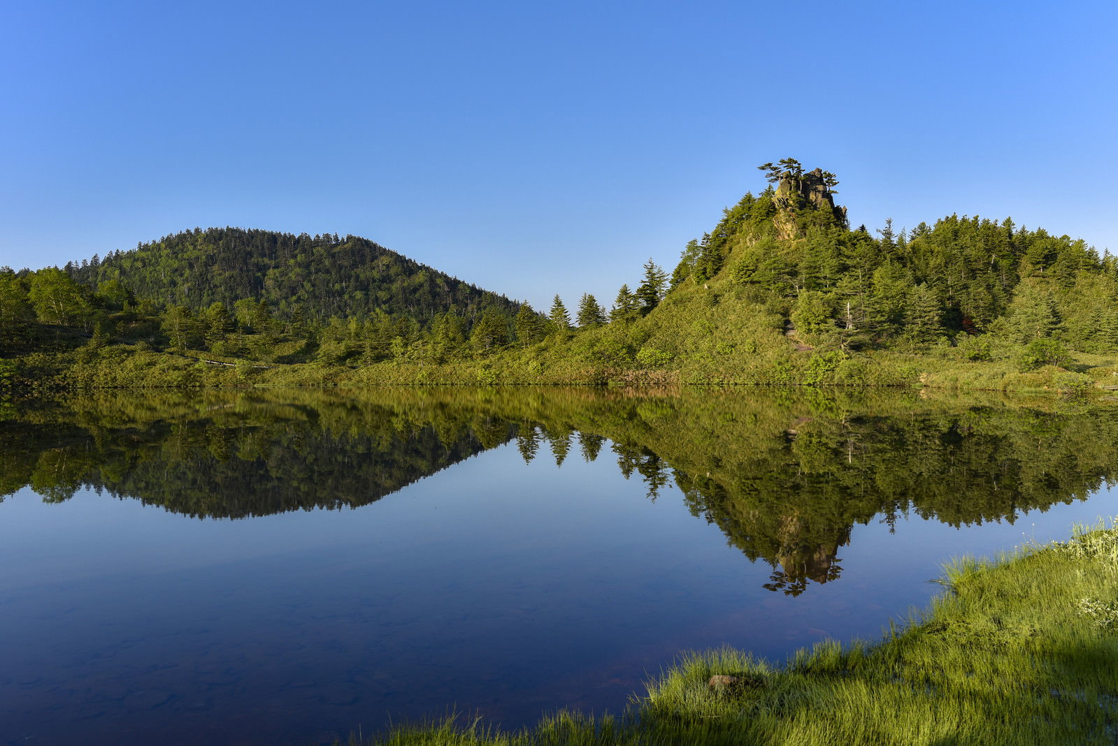 草津白根山の弓池で湖面に山々と青空が反射している自然風景