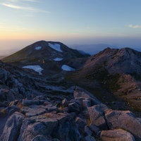 夕焼けに染まる白山の大汝峰と剣ヶ峰、岩場と山肌のグラデーションの写真