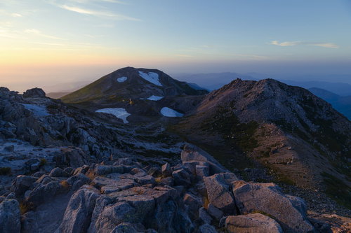 夕焼けに染まる白山の大汝峰と剣ヶ峰、岩場と山肌のグラデーション