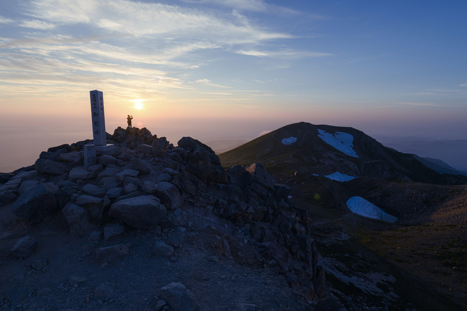 白山御前峰の山頂碑前で夕日を眺める登山者のシルエット