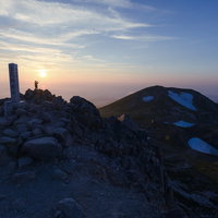 夕日に染まる白山御前峰の山頂碑と登山者たちの写真