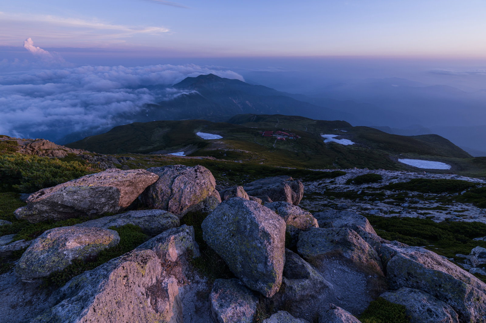 夕焼けに染まる空の下、岩場から望む白山室堂方面の山岳風景