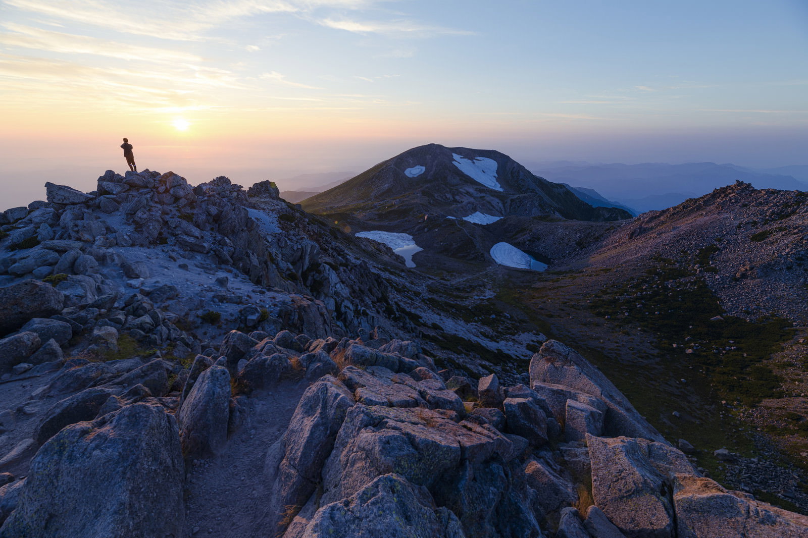 白山御前峰の岩場で日本海に沈む夕日を眺める登山者のシルエット