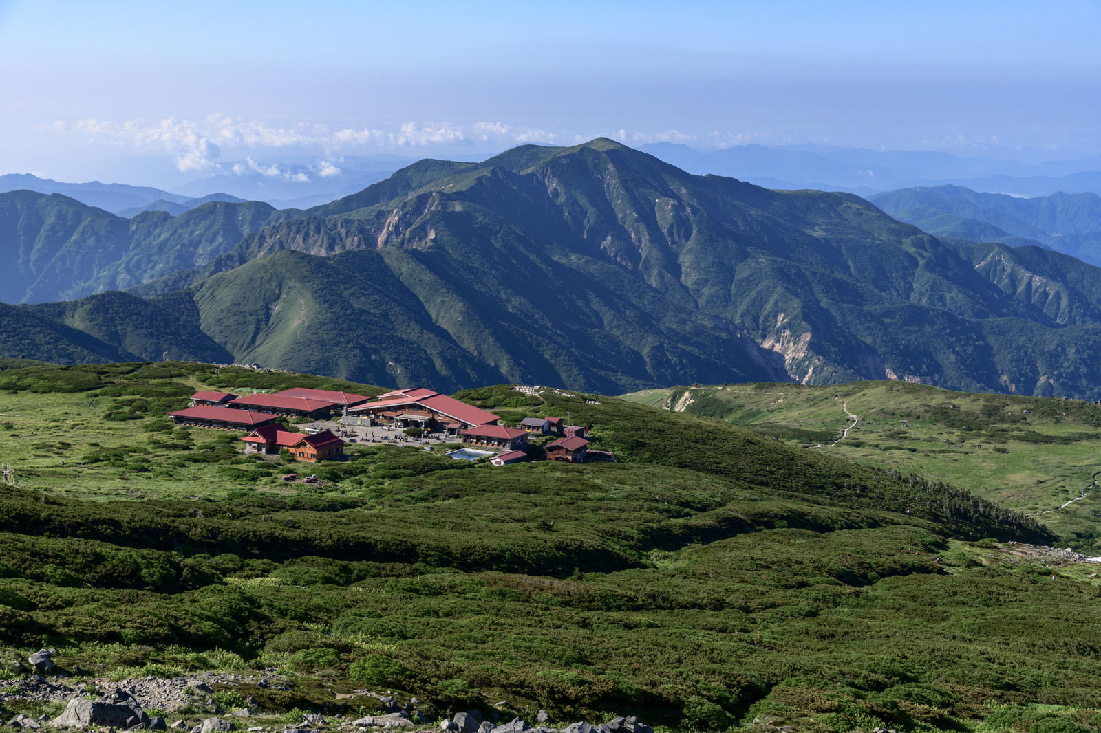 白山室堂平の緑の高原に建つ赤い屋根の山荘と背景に聳える別山の山並み