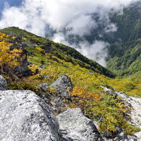 秋の紅葉に染まる鳳凰山の山肌と岩場の登山道の写真