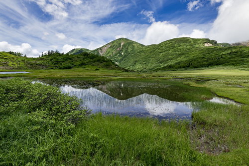 天狗の庭の池塘に映る青空と雲、背景に火打山（ひうちやま）