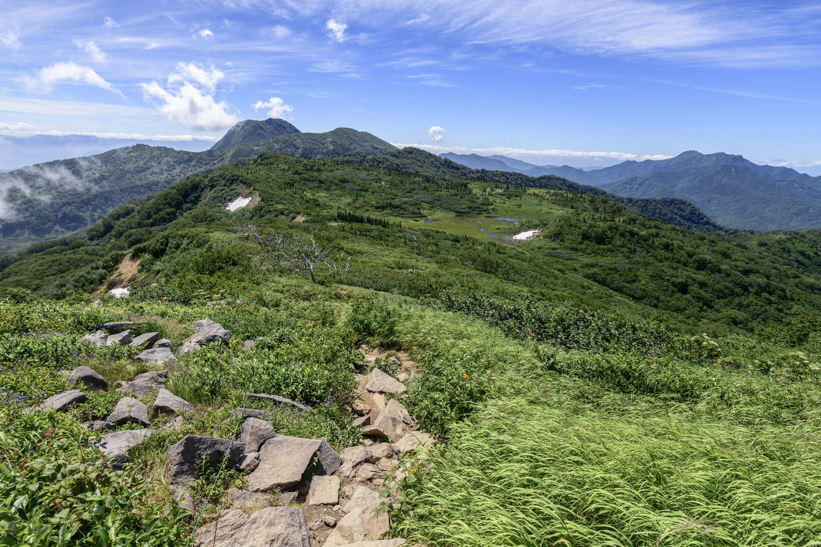 火打山稜線から妙高山を望む山岳風景、緑の登山道が続く