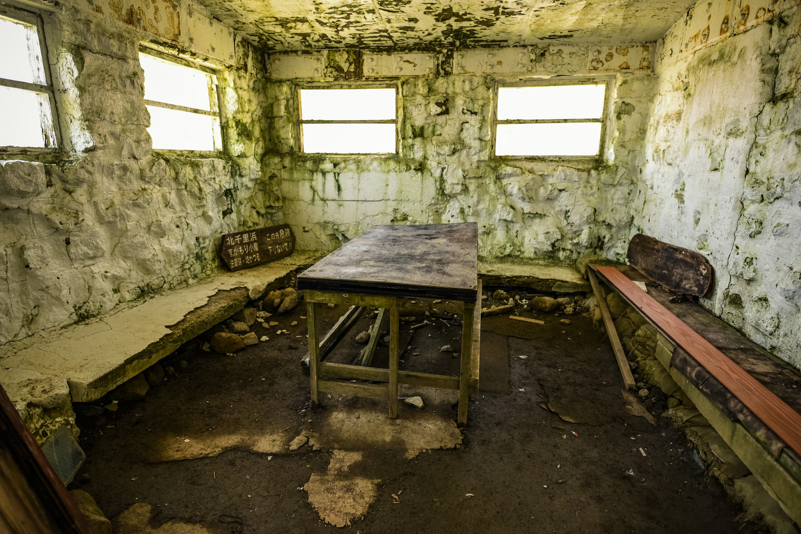 薄暗く朽ちた久住山避難小屋の内部、木製ベンチと剥がれた壁