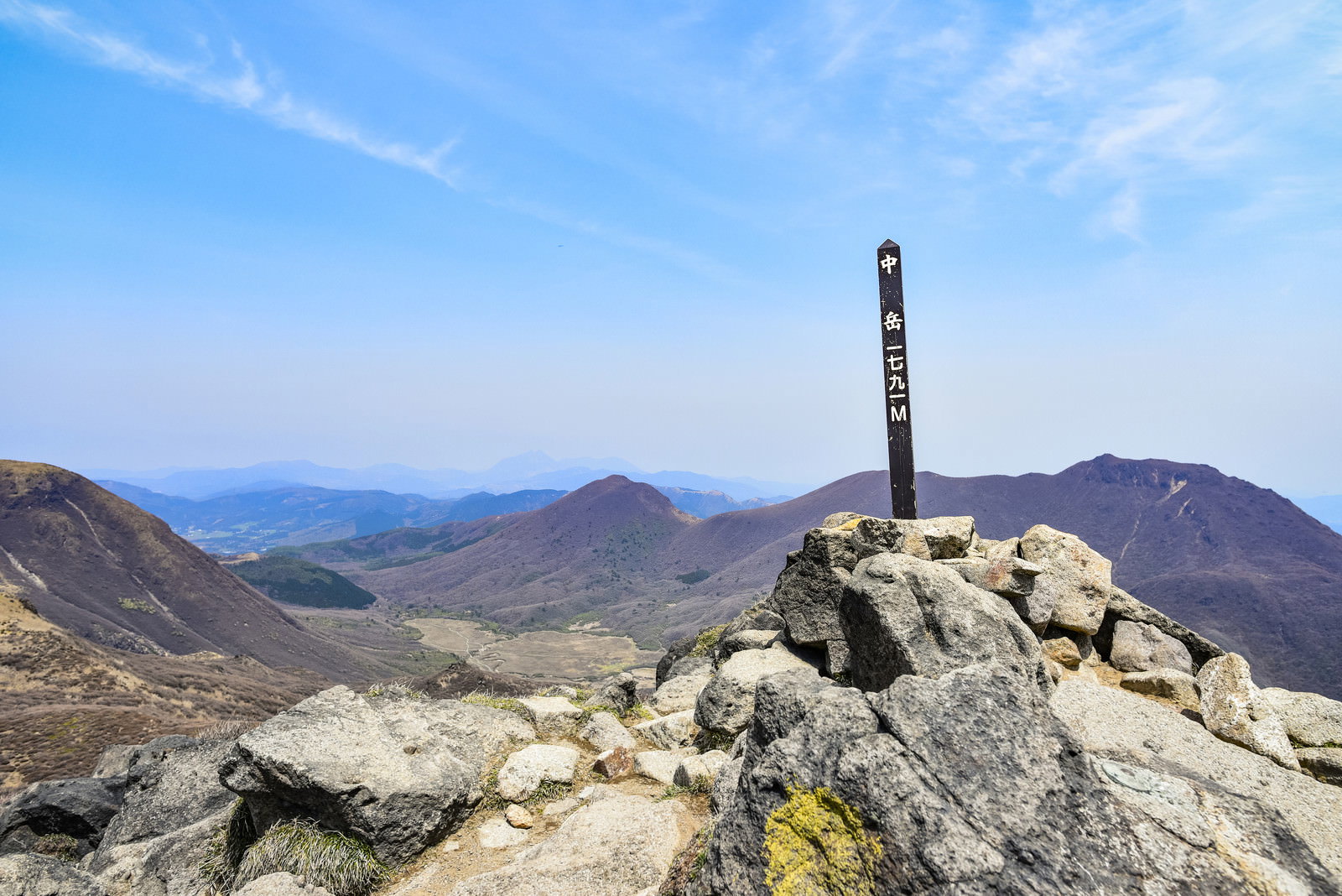 久住山中岳山頂に立つ山頂標と青空、背景に九重連山