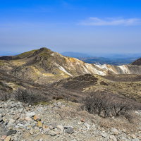 岩と枯れ木が点在する春の久住山、100名山の火山地帯の写真
