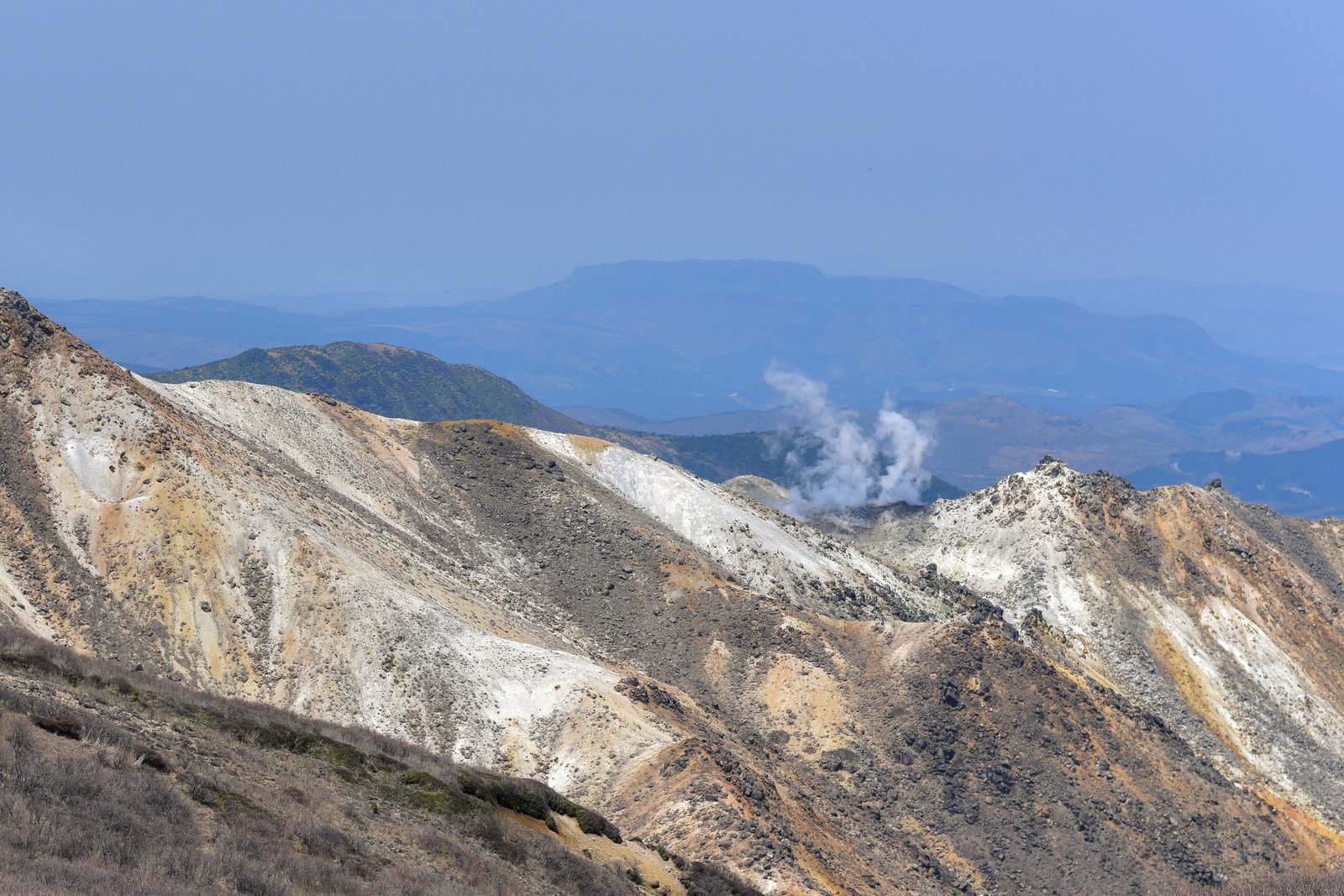 白い煙を上げる久住山の稜線と背景に広がる山々の風景