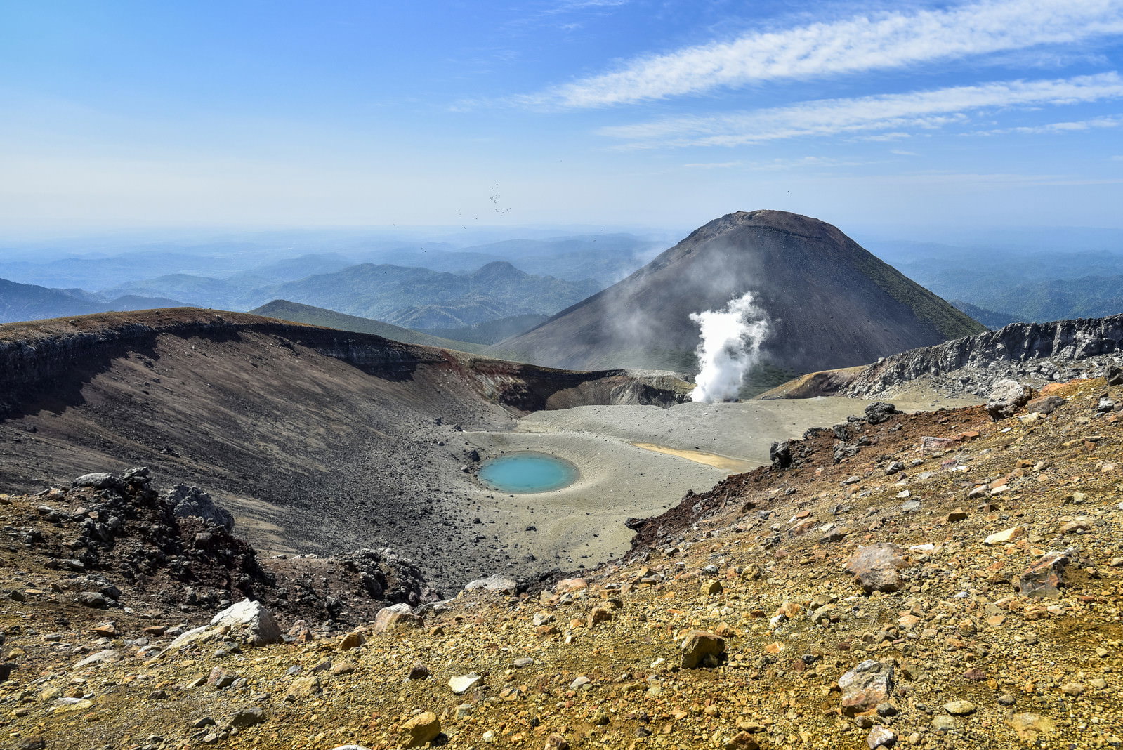 噴煙を上げる雌阿寒岳の山頂と手前に広がる青池の山岳風景
