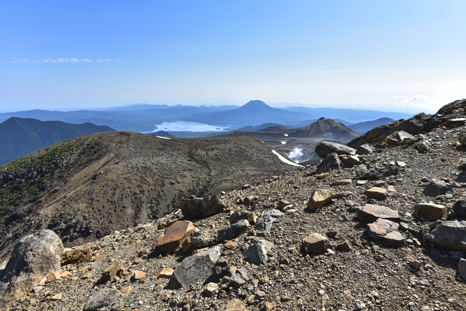 瓦礫が散らばる雌阿寒岳山頂から見える青空と山並みの風景
