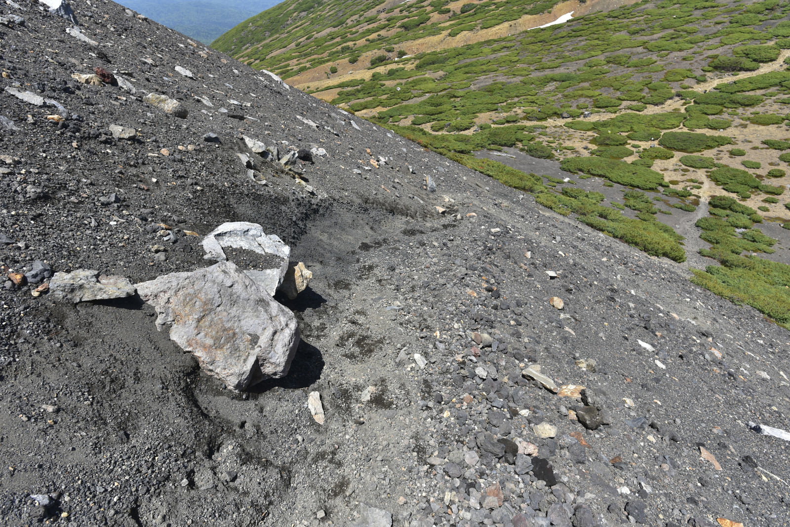 阿寒富士中腹の砂礫斜面を登る登山道と背景の緑の山々