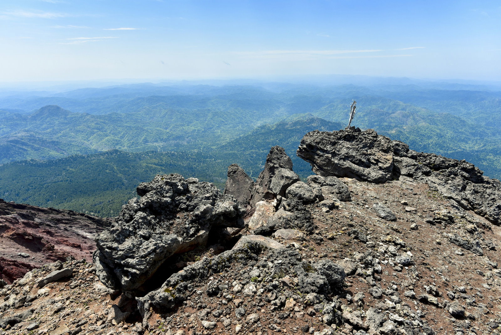 阿寒富士山頂の岩場から地平線まで続く緑の森林を見下ろす風景
