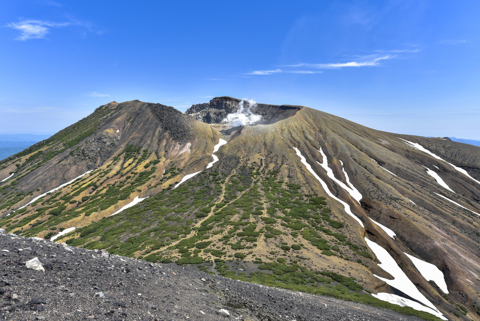 青空の下、阿寒富士山頂から眺める雌阿寒岳の雄大な山容と残雪