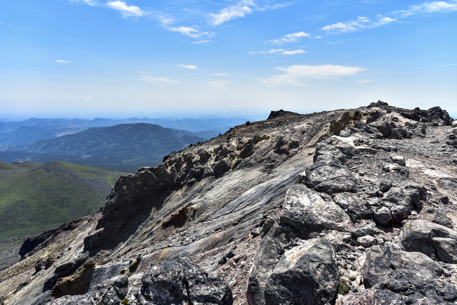阿寒富士山頂の溶岩が固まった岩場と遠方の山並み