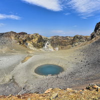 雌阿寒岳の火口中央にぽつりとある青池と火山地形の写真