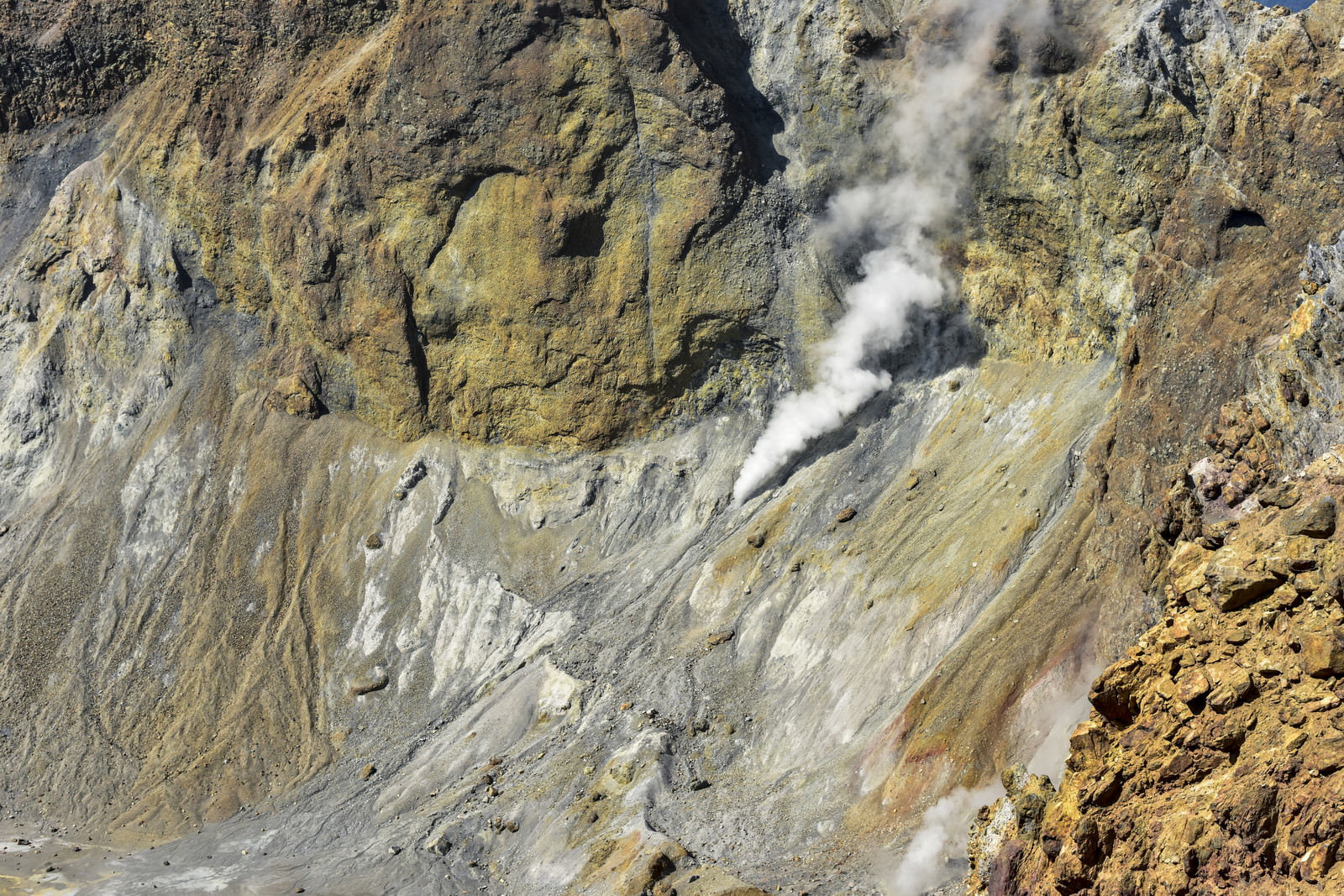 雌阿寒岳の火口から白い水蒸気を上げる噴気孔と茶色い岩肌