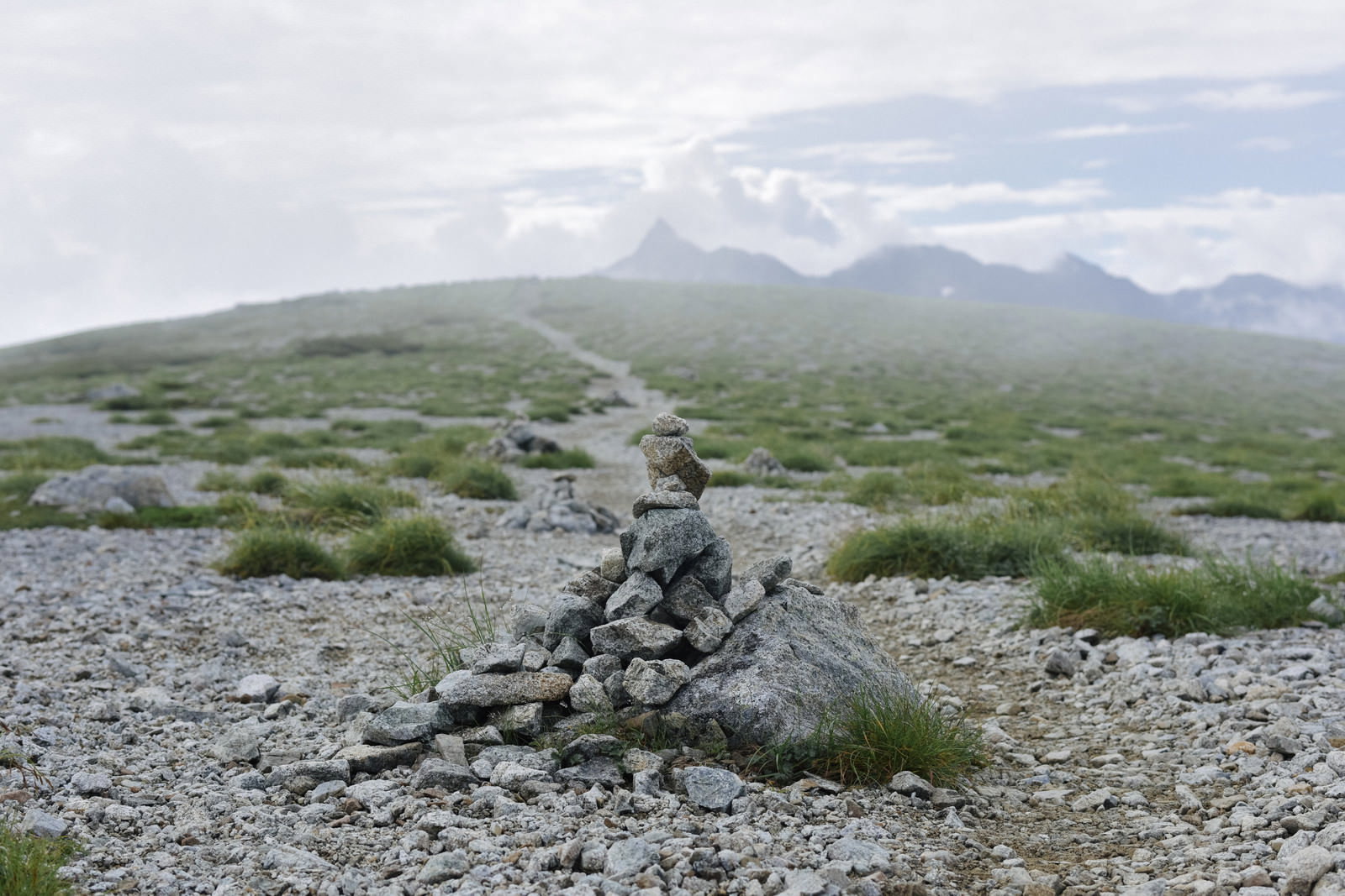 双六岳山頂に積まれた石のケルンと霧の向こうに見える槍ヶ岳