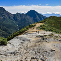 赤岳を背景に硫黄岳の稜線を登る登山者たちの写真