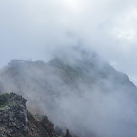 雲の中にうっすらと姿を見せる日本百名山の赤岳と山小屋の写真