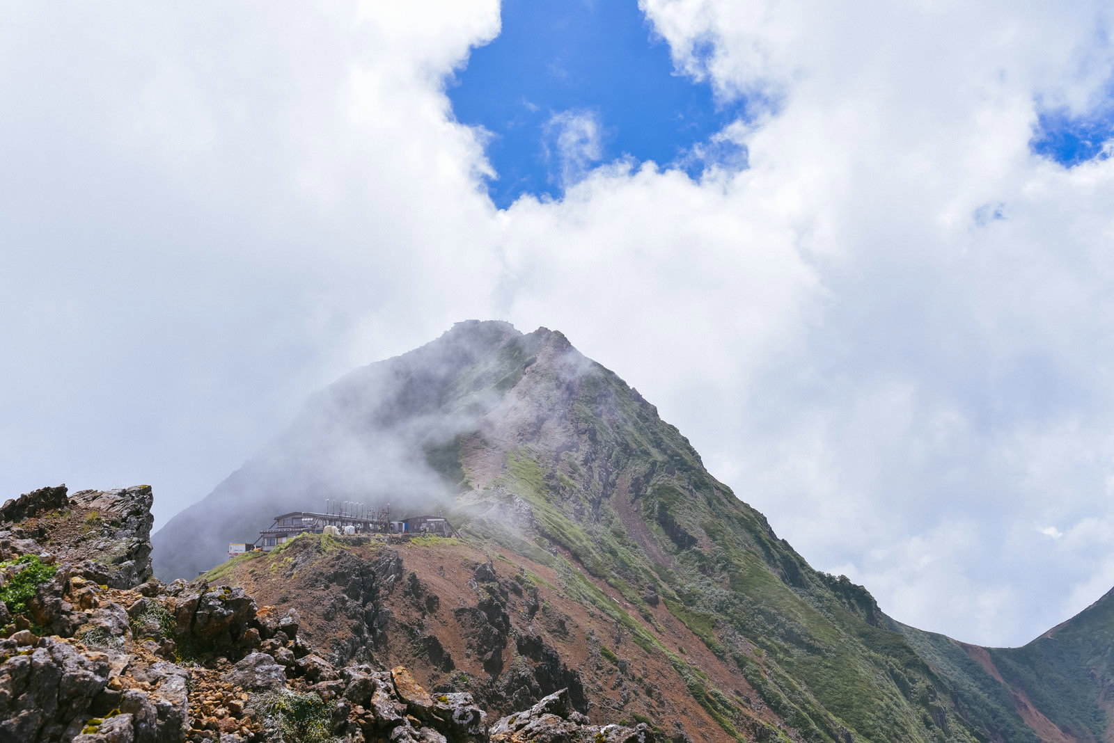 雲に包まれながらも青空の下に顔を出す赤岳山頂の様子