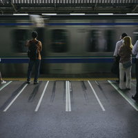 駅のホームで通勤電車を待つ朝の乗客たちの写真