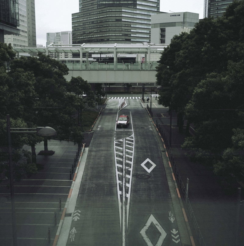 高層ビルに囲まれた都市の道路を走るタクシーと街路樹