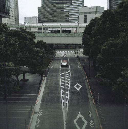 高層ビル群の道路の中心へと吸い込まれてゆくタクシー