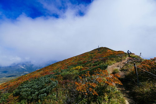 雲の合間に見える栗駒山の秋の紅葉と青空の風景