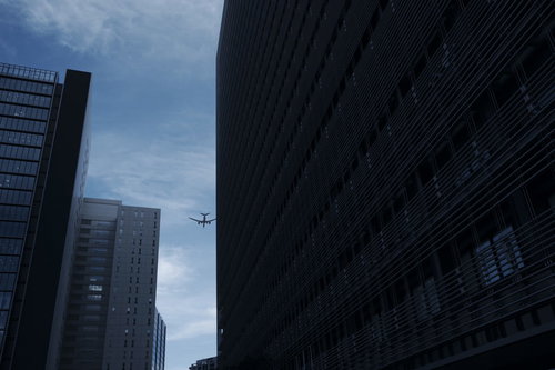 ビルの隙間の向こうへと跳んで行く飛行機のシルエット