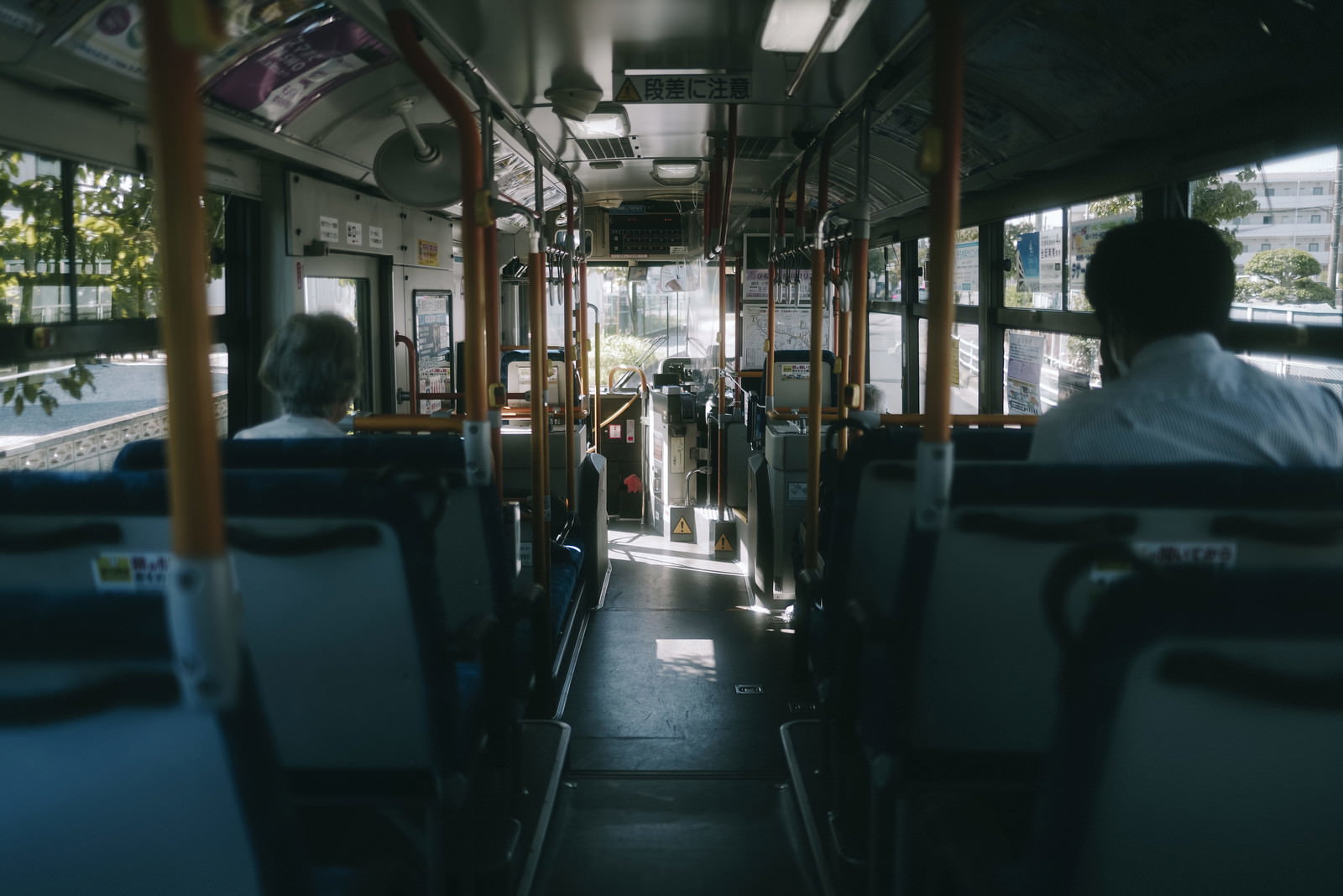 早朝の薄暗い通勤バスの車内、青緑色のシートが並ぶ様子