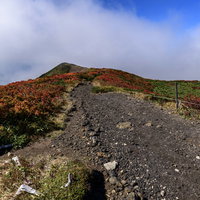 流れる雲の下に顔を見せる真っ赤な紅葉の栗駒山登山道の写真