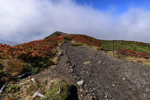 流れる雲の下に顔を見せる真っ赤な紅葉の栗駒山登山道