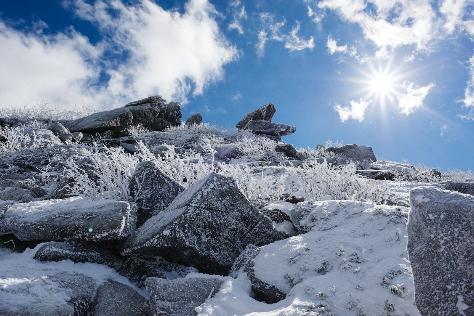 雪化粧した金峰山の稜線と岩場、青空に白い雲が流れる冬山の風景