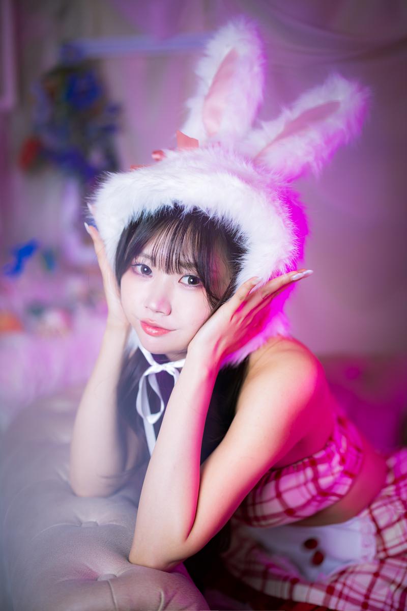 ピンク照明の中で白いウサギ耳のカチューシャをつけ、にっこり笑うバニー衣装姿の女性［モデル：れいか氏］