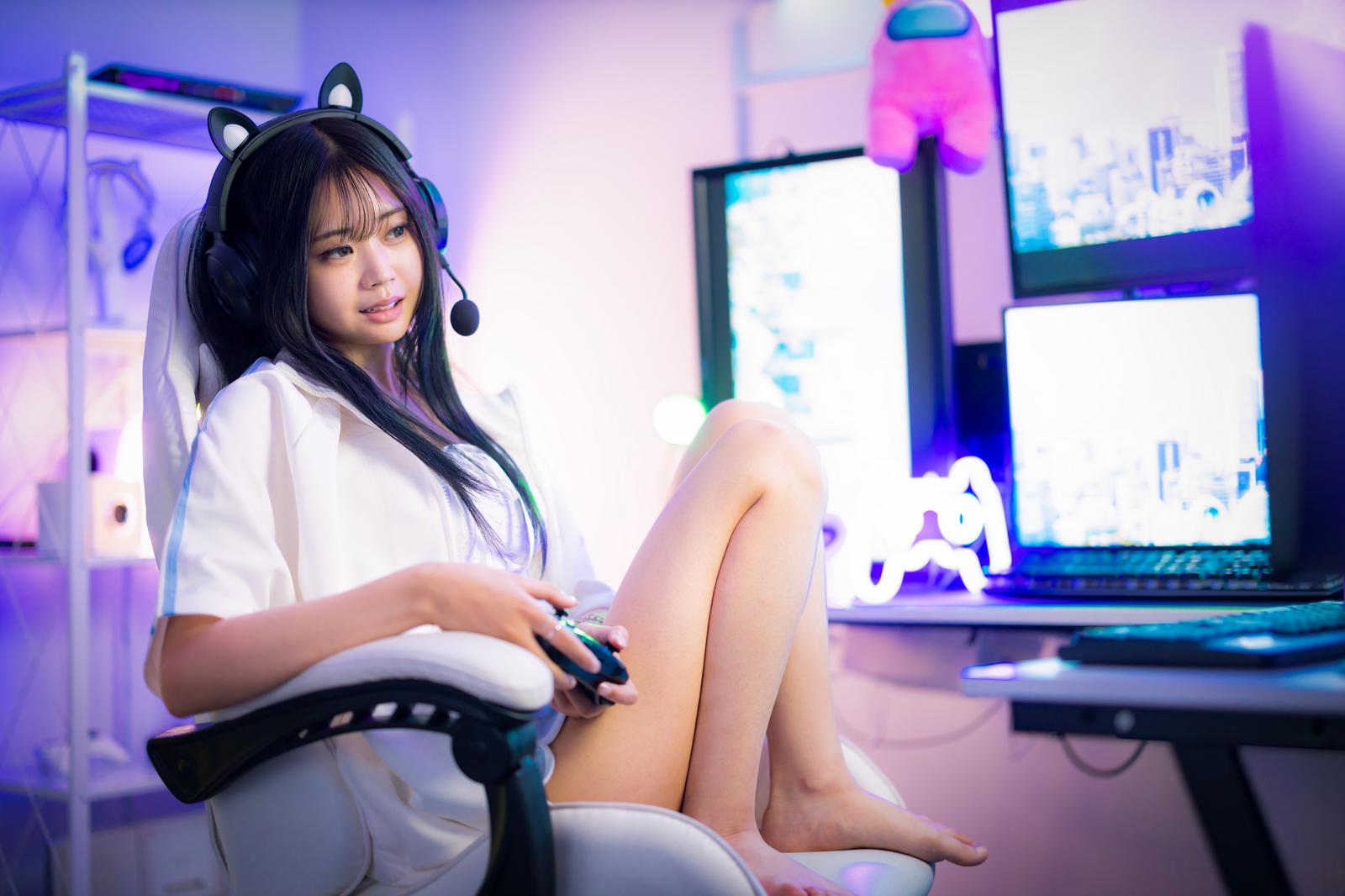複数のディスプレイの前でゲームコントローラーを持つ猫耳ヘッドセット姿の女性［モデル：れいか氏］