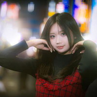 光あふれる繁華街のネオンを背に髪をあげる若い女性の写真