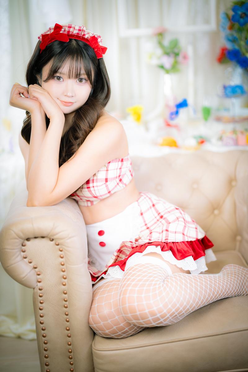 赤いリボンのヘアバンドをした女性がメイド服でソファーに座っている［モデル：れいか氏］