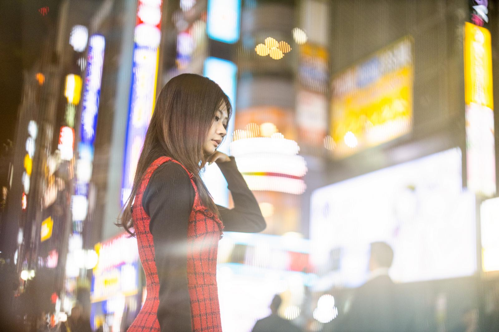 Portrait of a woman in a red checkered one-piece dress with her hand to her hair against neon lights in a bustling downtown area at night