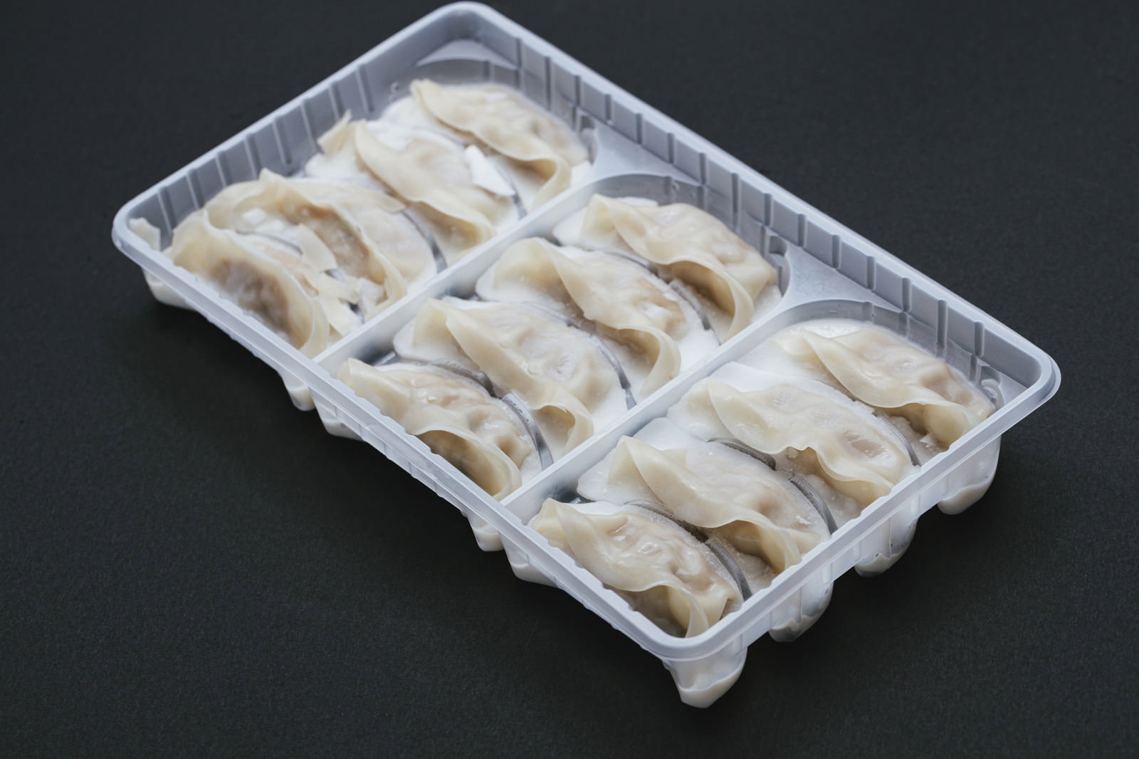 透明なプラスチックパックに整然と並べられた白い冷凍餃子